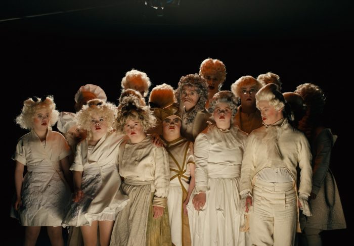 Scènefoto uit de voorstelling Furia van KamaK. Een groep acteurs met barokachtige kostuums staat dicht bij elkaar, de meesten kijken naar de camera